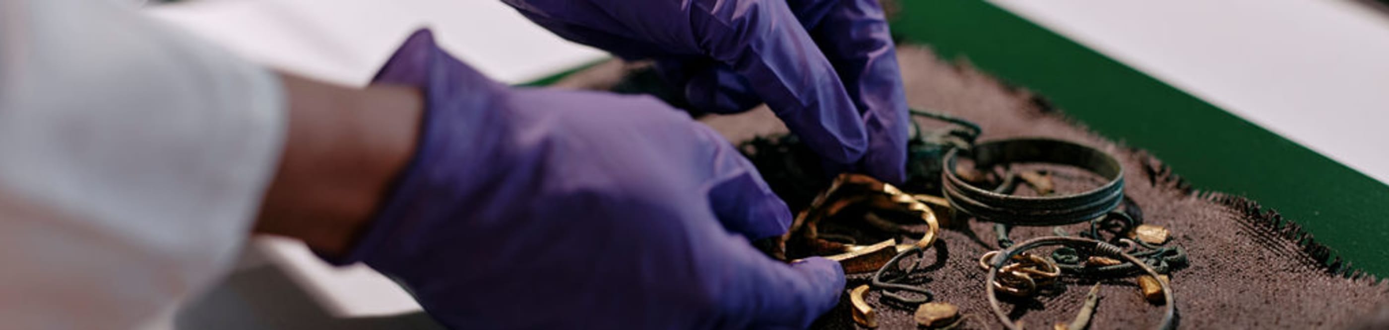 Person in white coat and purple protective gloves puts a display of gold and metal jewellery in a case