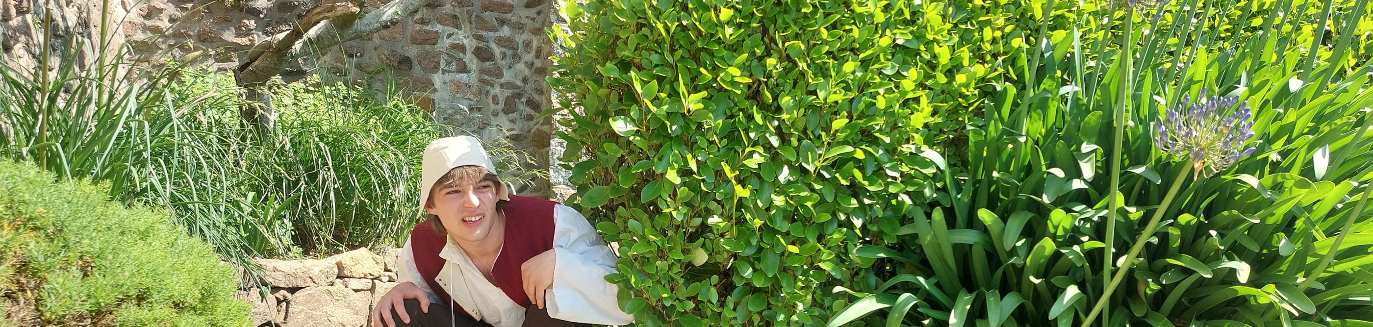 Man in serf costume hides behind a plant at a castle