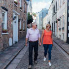 A couple dressed for summer walk towards camera down a narrow street.