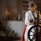 Women in 17th century costume sits at a spinning wheel