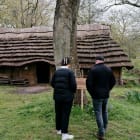 Two people read sign inf front of a replica neolithic longhouse