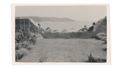 Two people relax on a wall overlooking a coast