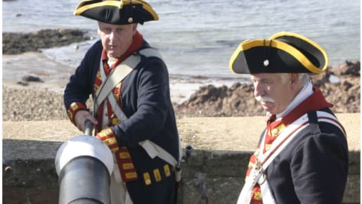 Two men in uniform stick a long pole into a cannon