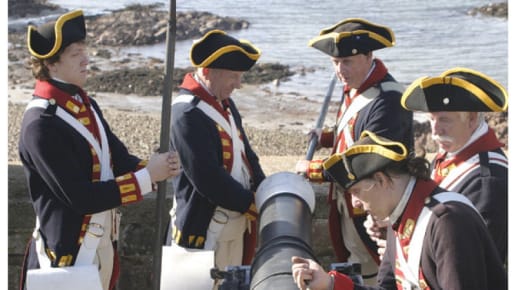 five men in uniform watch as one puts black powder into a cannon
