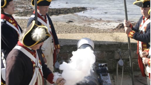 four men stand around a cannon as smoke comes from the lit fuse