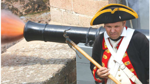 a man in uniform walks away from a cannon firing with shot coming out the front of the cannon