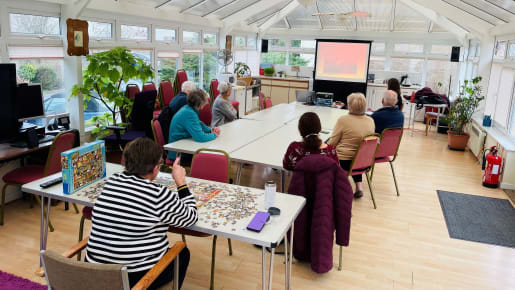 A small group of people watch at talk in a glass roofed building