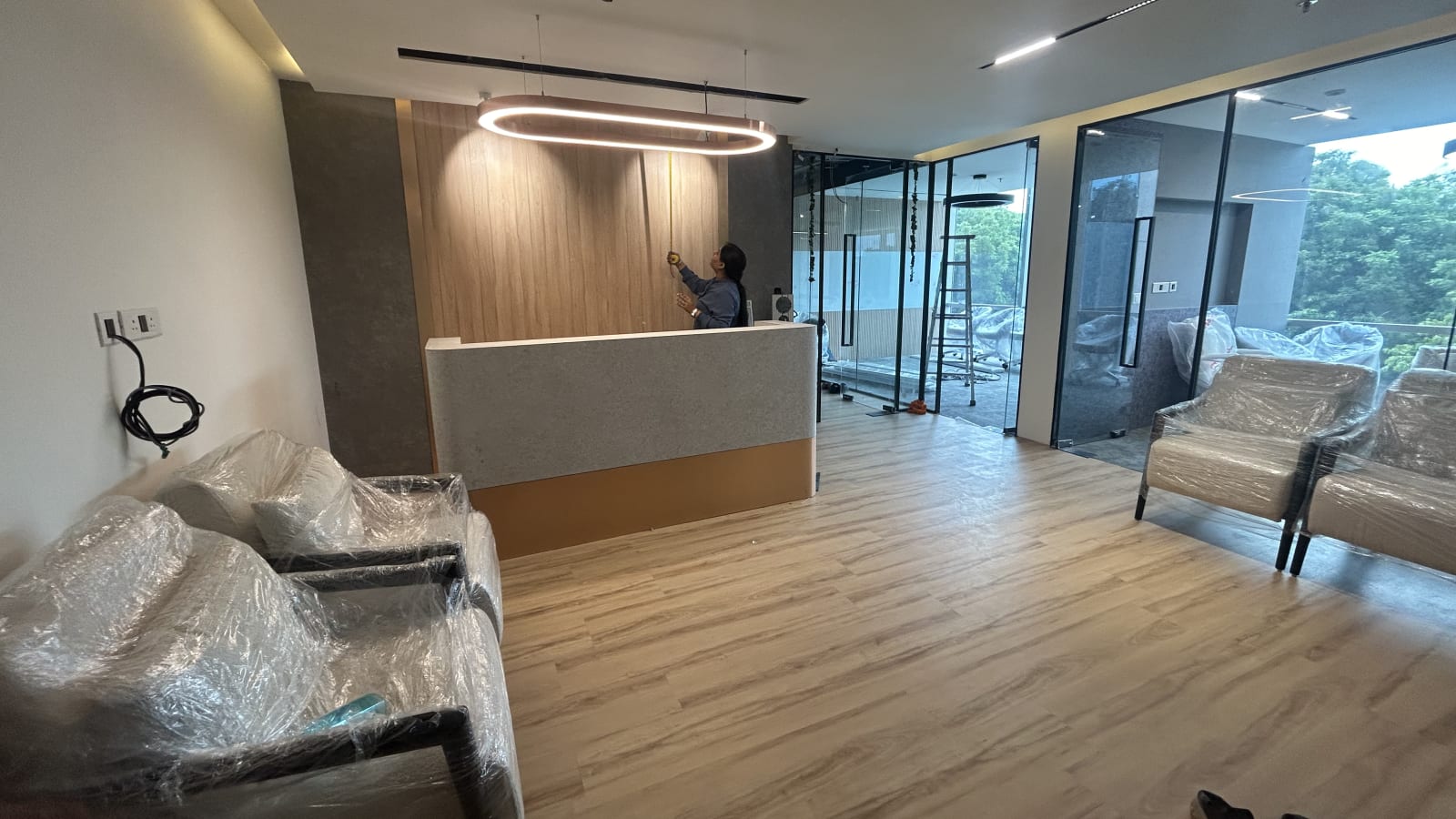 Reception desk with timber panelling and a ring pendant light beside glass-fronted meeting rooms in an Officea Design & Build office fit-out