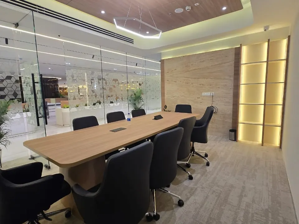 Meeting room with a long wood-top table, a stone-clad wall, backlit shelving and frosted glass partitions