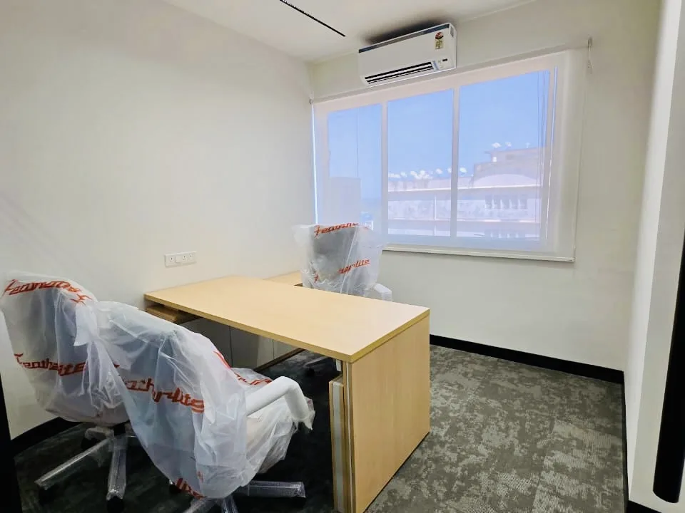 Newly fitted office cabin with a light wood desk, a wall-mounted split air conditioner and chairs still in protective wrap before handover
