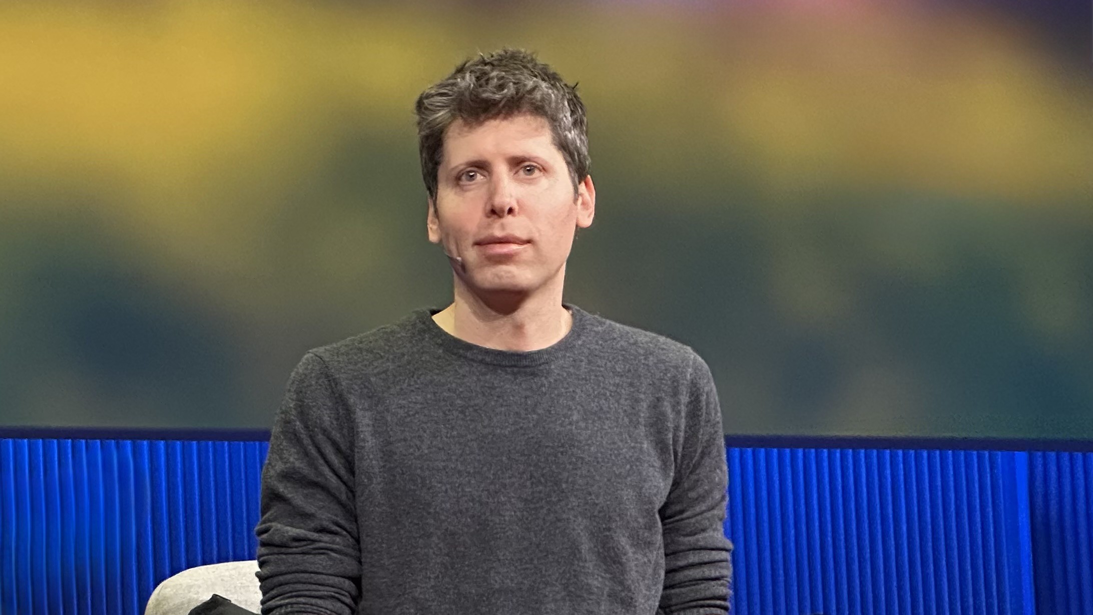 Sam Altman, OpenAI's CEO, in a grey sweater, looking at the camera