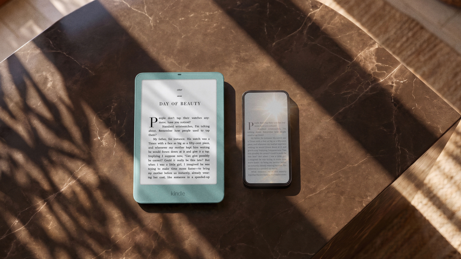 Seaglass Green Kindle Paperwhite showing clear book text next to a smartphone washed out by sunlight glare on a marble table