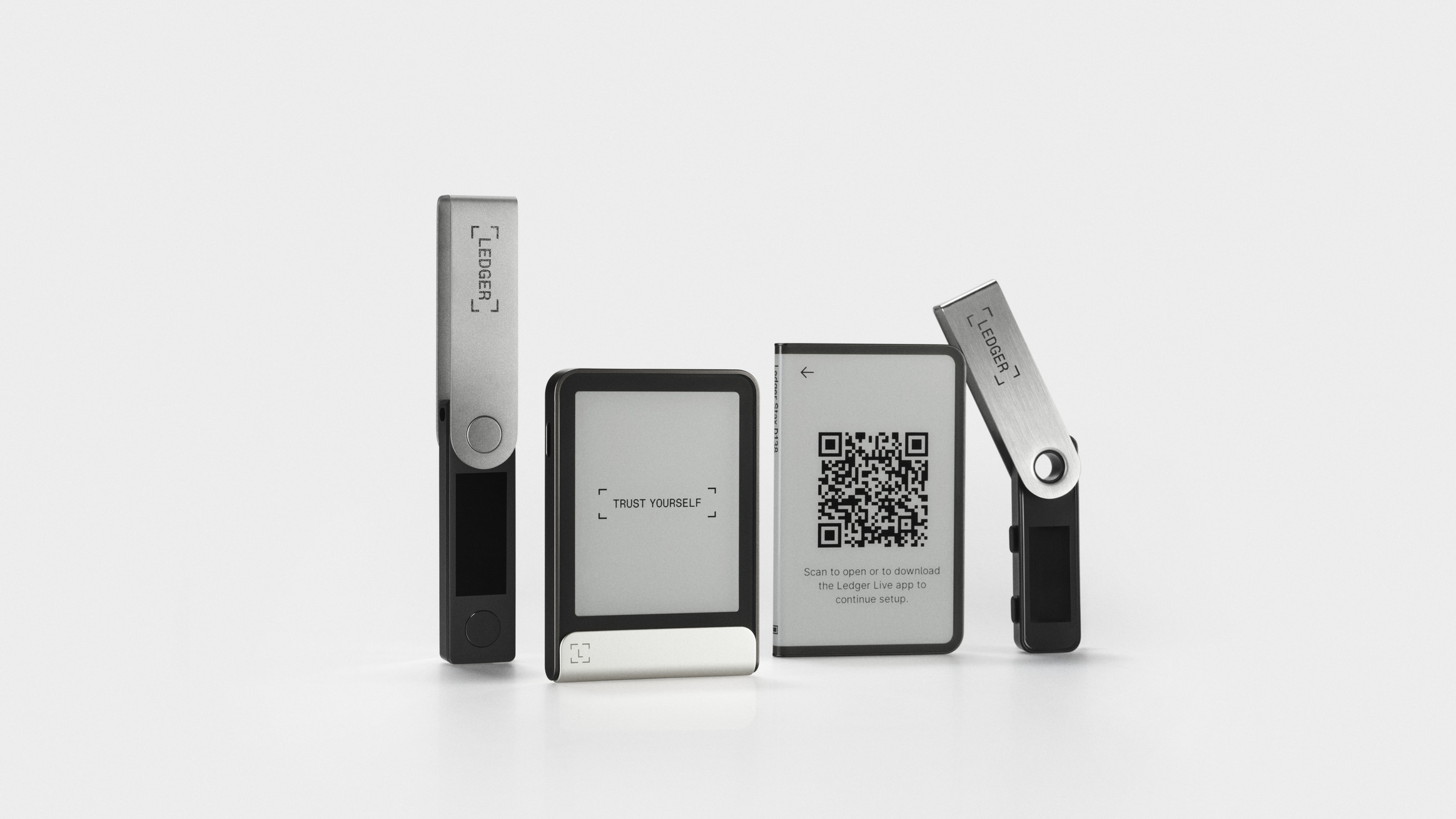 Official Ledger product shot of four Ledger hardware wallets standing on a white surface: two USB-stick-style Nano models with swivel covers on the outside and two card-style touchscreen models in the middle, one reading Trust Yourself and one showing a setup QR code