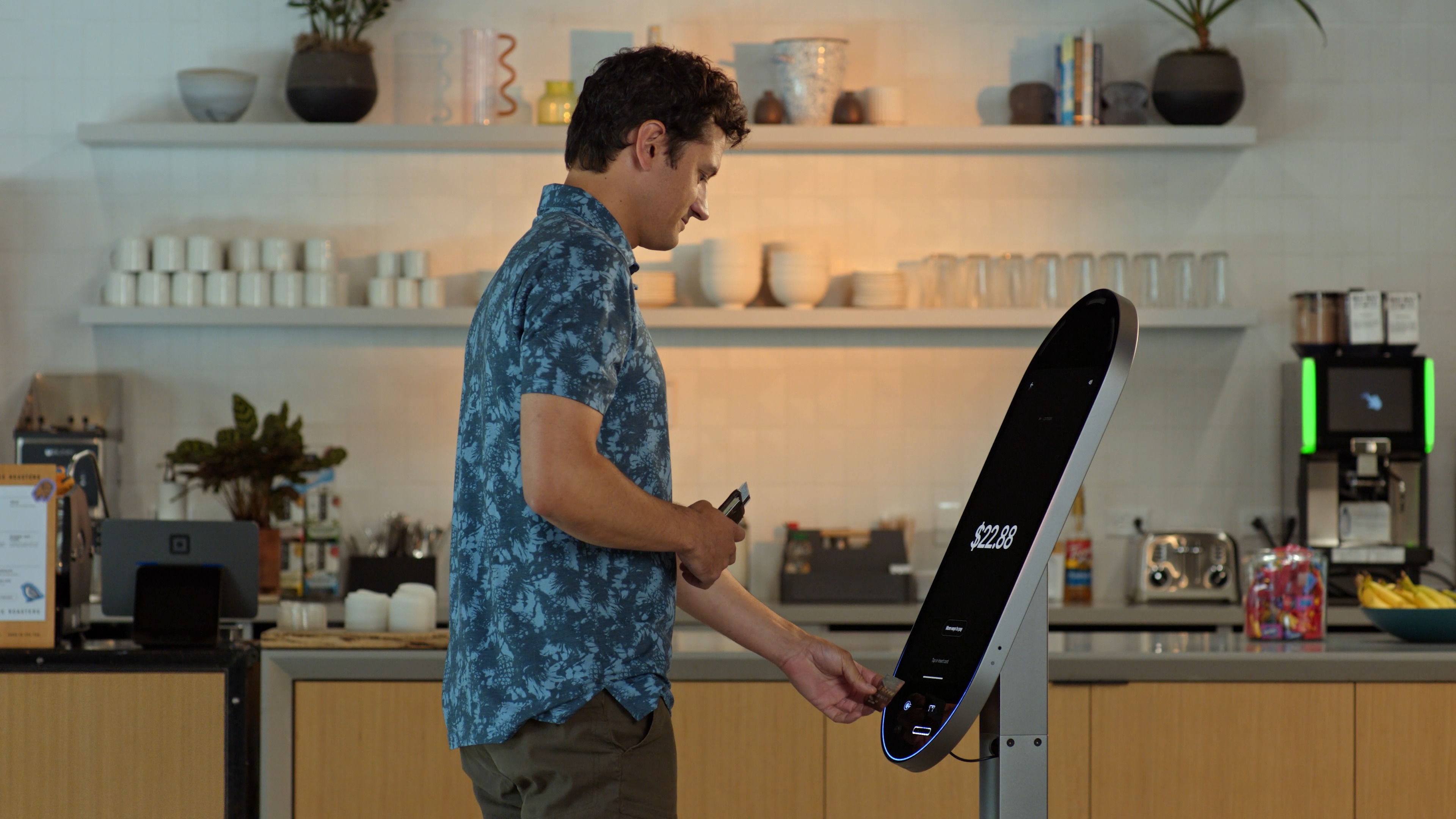 Customer paying by tapping a card on a Square Kiosk floor stand showing a $22.88 total in a cafe
