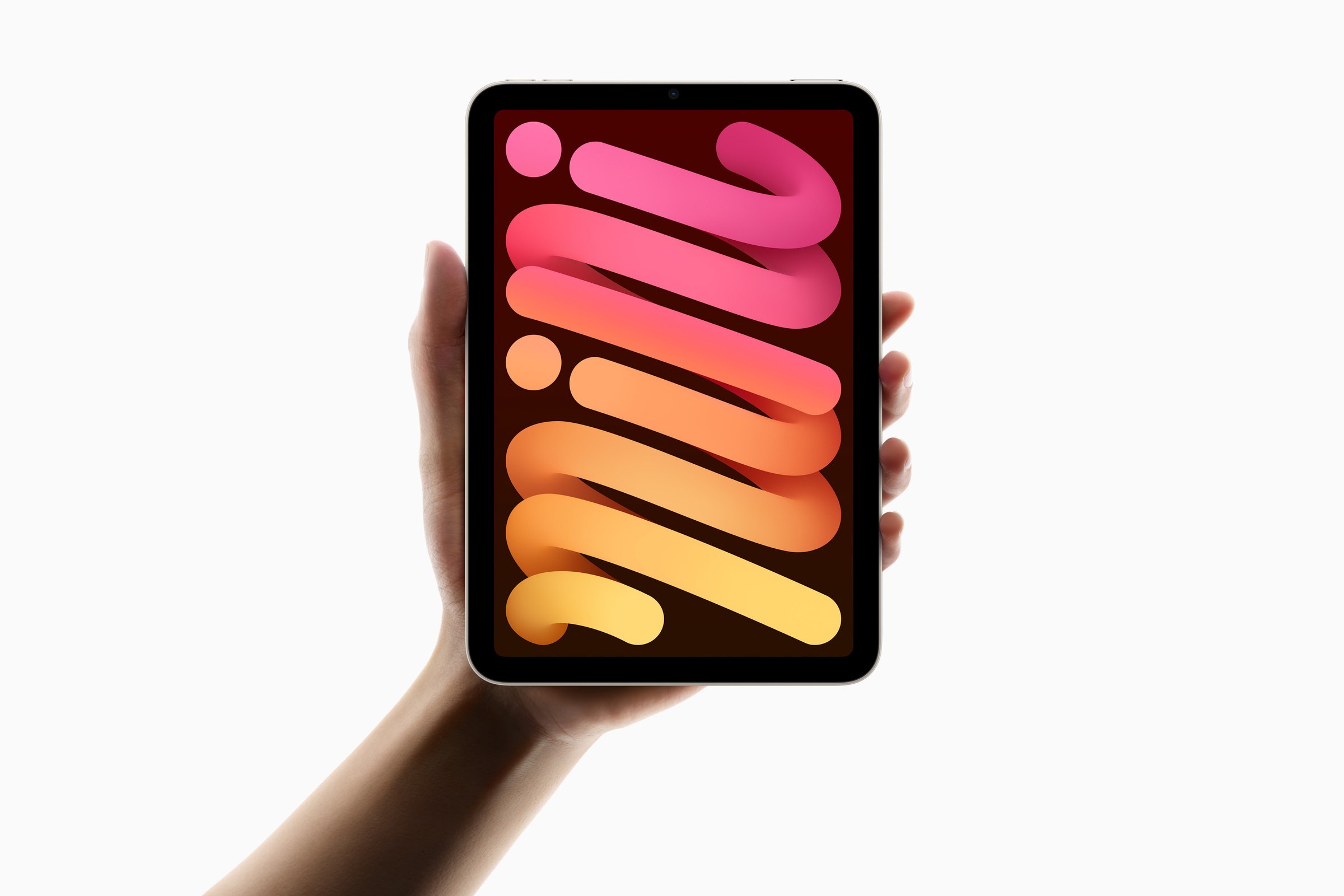 A hand holding the current iPad mini in starlight, showing a pink and orange wallpaper on its 8.3-inch screen