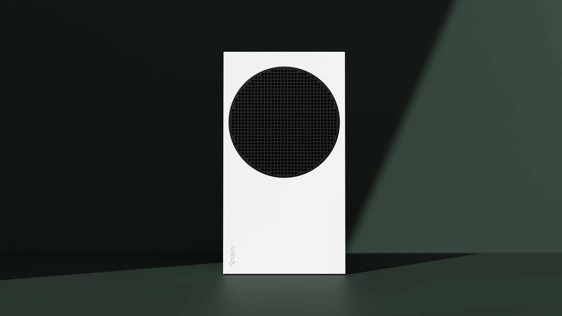 White Xbox Series S console standing upright against a dark green wall, with its round black vent facing the camera
