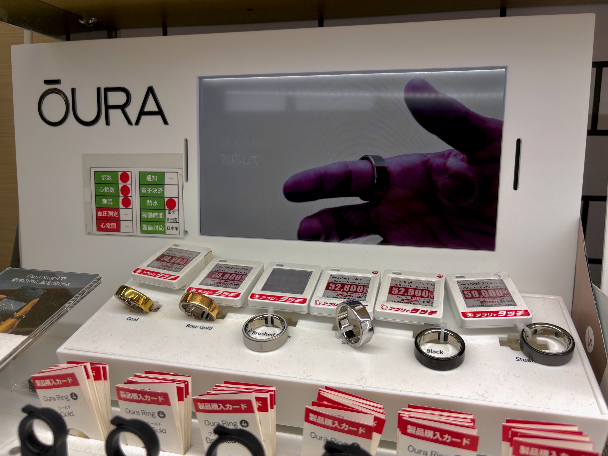 Oura Ring 4 smart rings in gold, rose gold, silver, black and stealth on a store display with electronic price tags