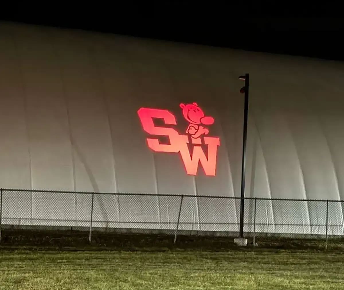 School initials with a cartoon mascot beamed onto a white sports dome at night — Infinity Projectors