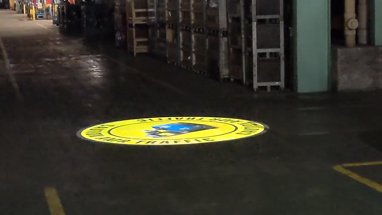 Projected CAUTION AMR TRAFFIC safety sign on a real warehouse floor — Infinity Projectors safety sign projector