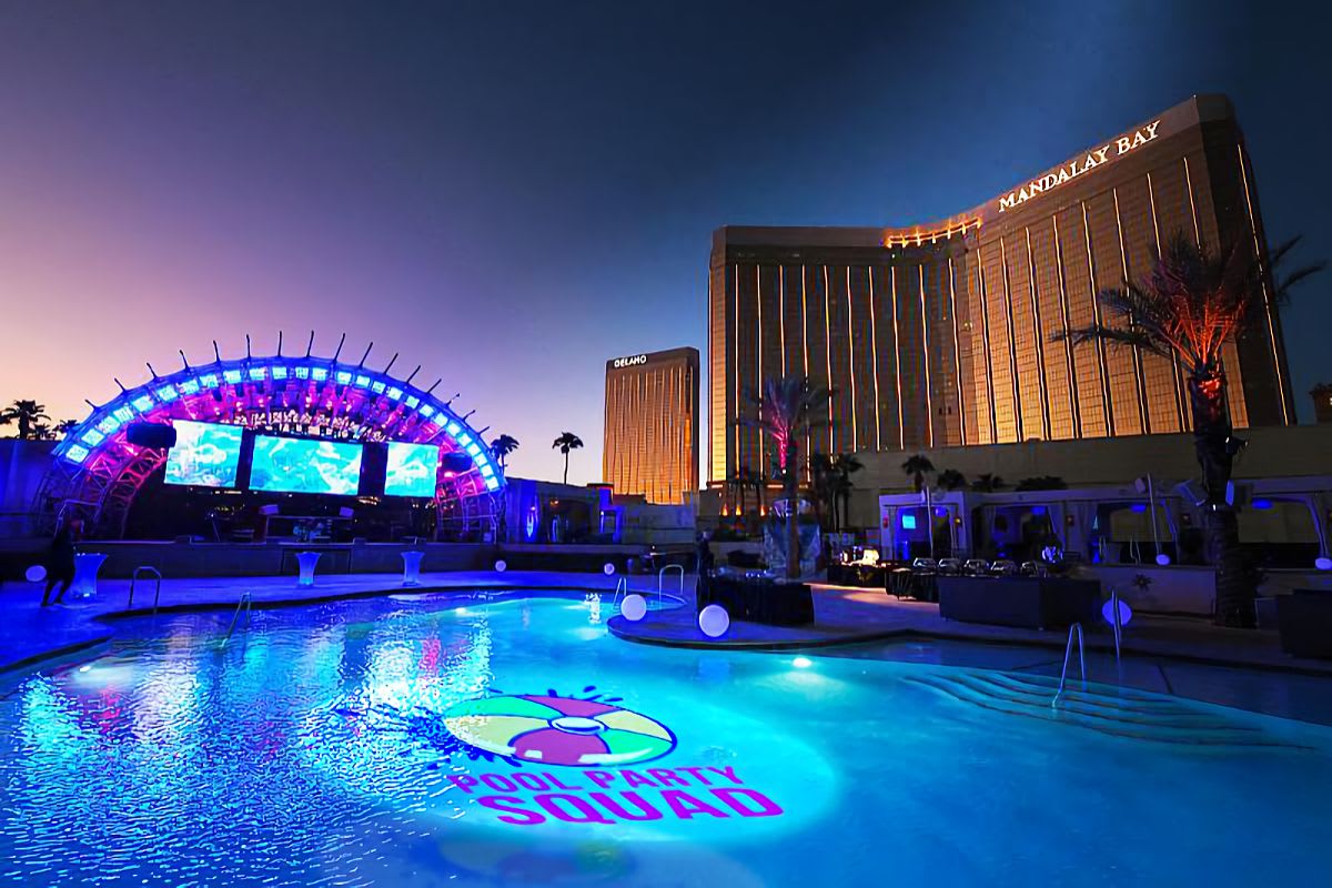 Beach-ball party logo projected onto a resort pool at dusk beside a stage — outdoor logo projector in action