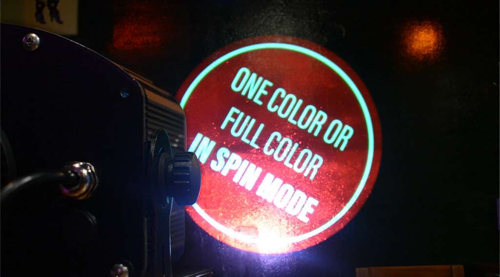 Rotating gobo projector up close, beaming a red full-color spin mode demo on a dark wall