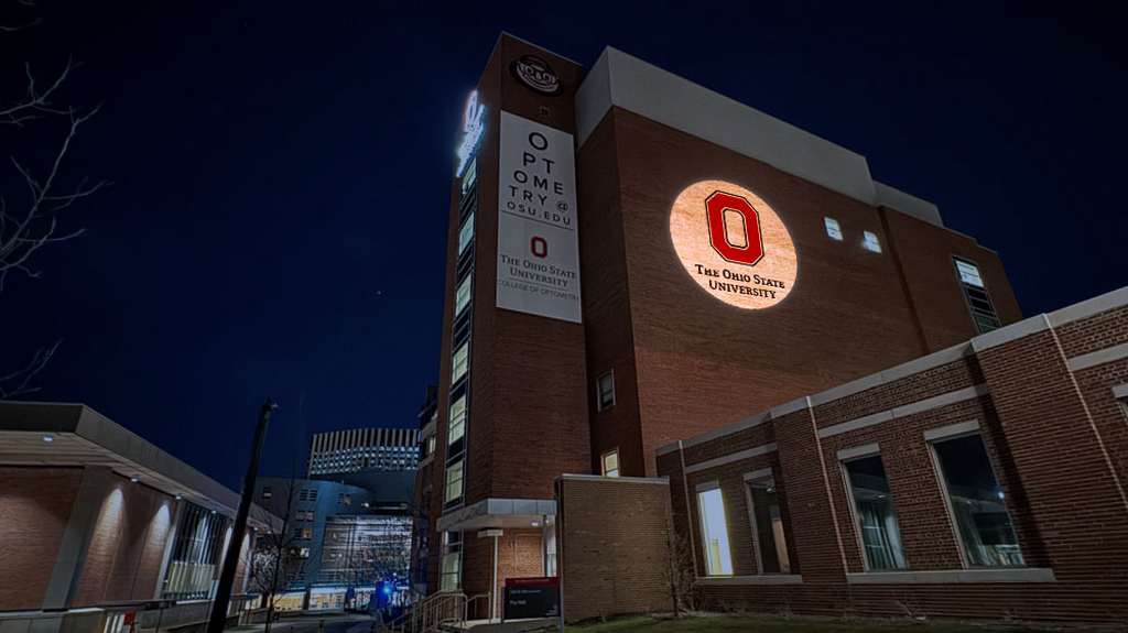 University logo projected in a warm circle on the brick tower of a campus building at night — Infinity Projectors