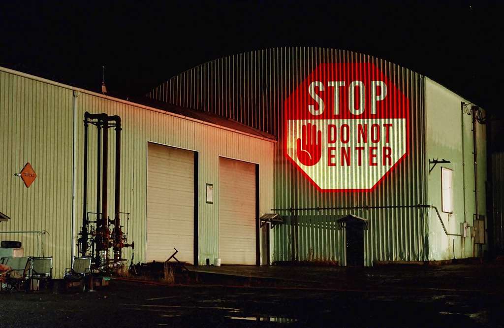 Red stop do-not-enter gobo covering the corrugated wall of an industrial building at night