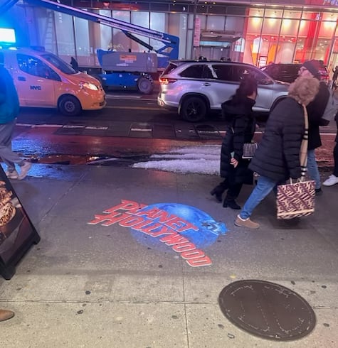 Full-color floor projection of a restaurant's globe logo on a busy city sidewalk at night