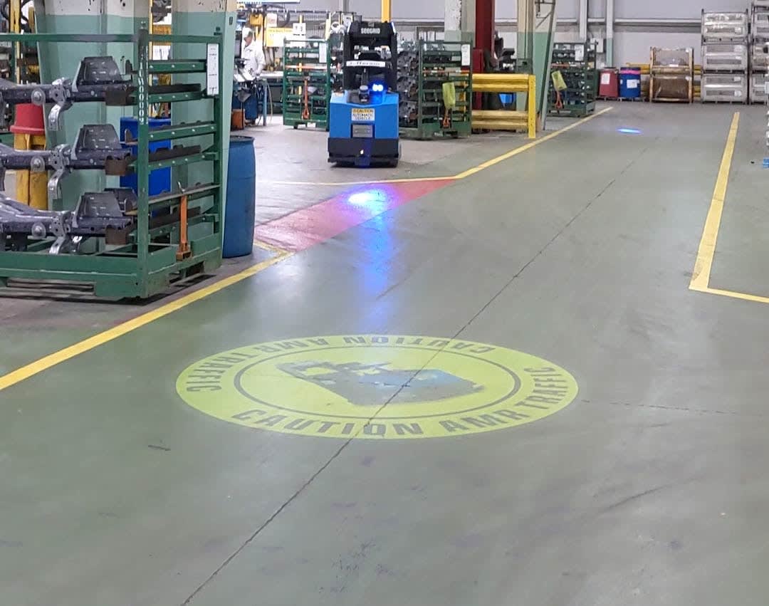 Video: yellow caution safety sign projected on a factory aisle floor as an automated forklift approaches