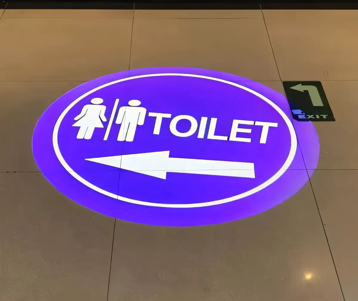 Purple toilet-direction gobo with restroom icons and an arrow shining on a polished mall floor