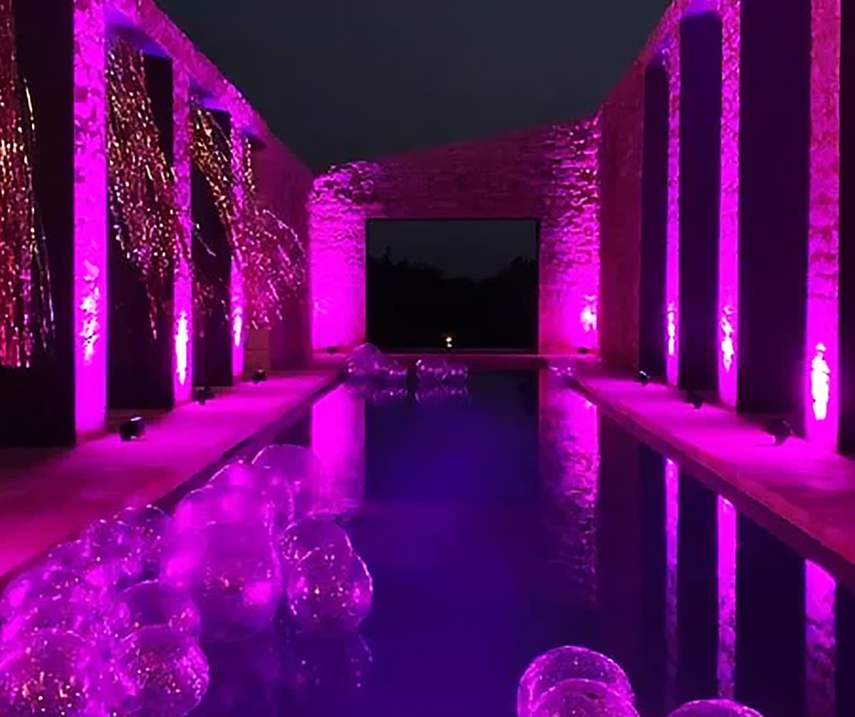 Stone colonnade and reflecting pool bathed in magenta uplight with glowing balloons on the water