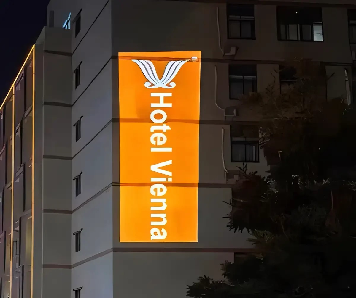 A hotel's name and winged emblem in a tall orange panel of light running down a building corner at night