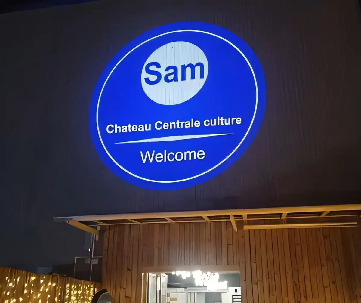 A venue's round blue Welcome greeting projected large on a dark wall above a timber-clad entrance after dark
