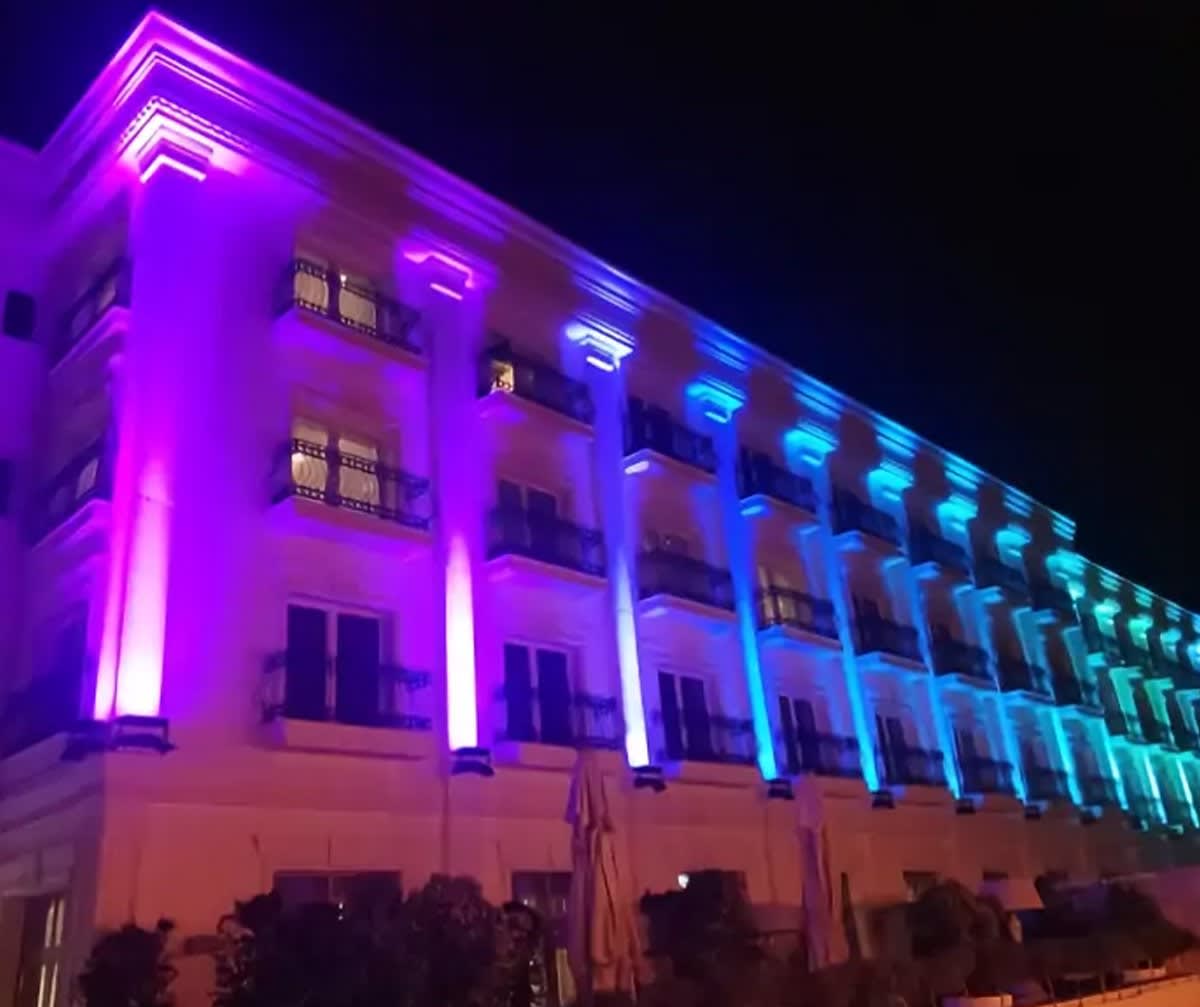 Classic hotel facade with columns alternately washed violet and sky blue above evening greenery