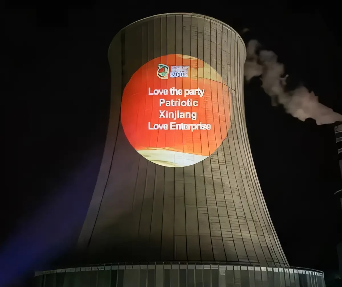 Orange circle of patriotic slogans lighting up a power plant cooling tower at night from a high wattage projector
