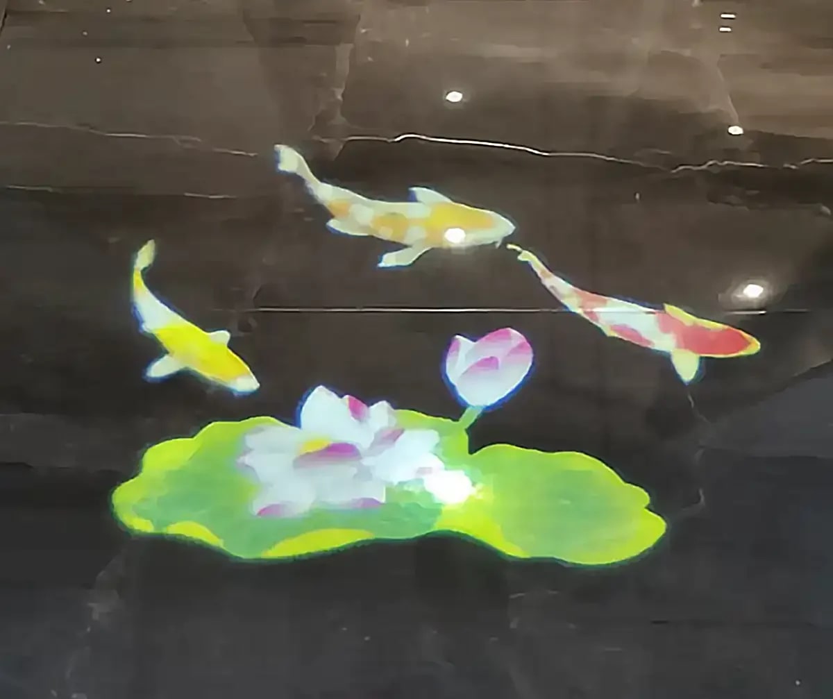 Colorful koi and lotus flower on a green lily pad glowing on black marble, a vivid full-color gobo scene