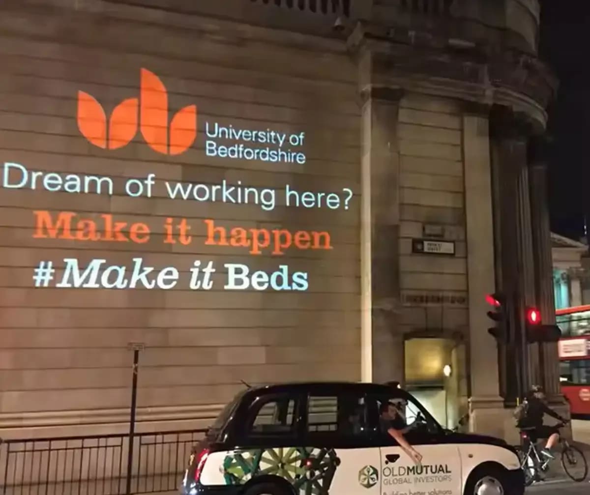 Recruitment message and leaf logo beamed onto a stone building facade at night from an outdoor logo projector