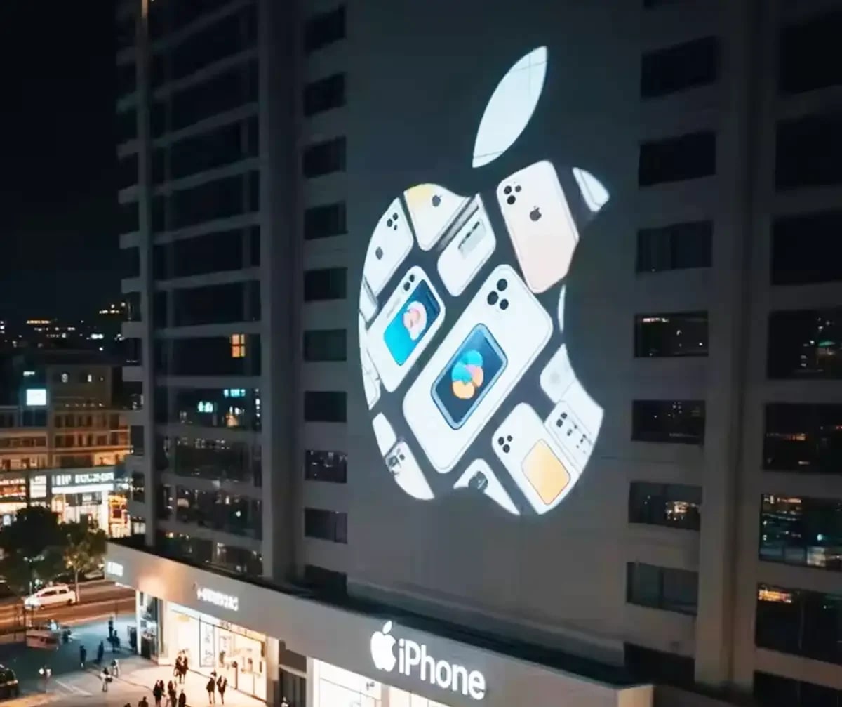 A tech giant's fruit logo formed from phone images projected on a high-rise above its brightly lit storefront