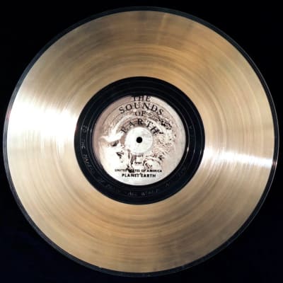 A golden vinyl record with a black label and text reading "The Sounds of Planet Earth" is displayed against a dark background.