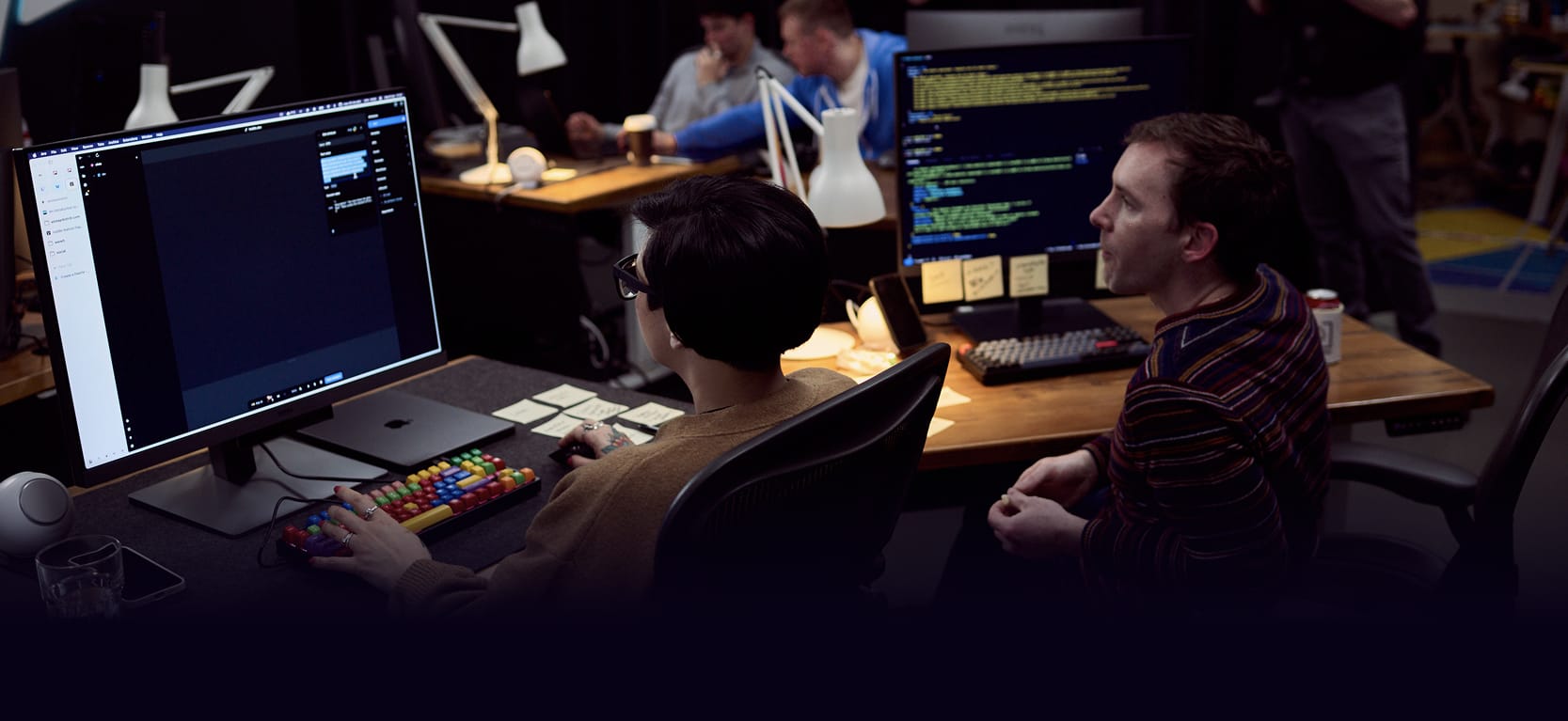 Salma Alam-Naylor and Daniel Roe on the set of Web Dev Challenge S2, looking at code on large monitors.