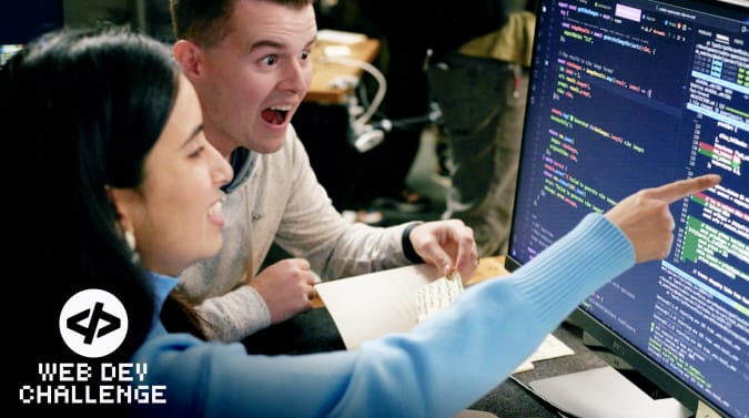 a woman points at code on a computer screen. a man sitting next to her leans forward and looks at the screen excitedly
