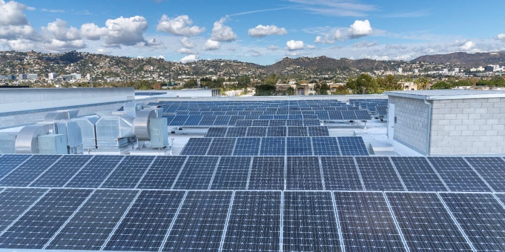 A sea of solar panels on a commercial real estate building with a city and mountain range in the background