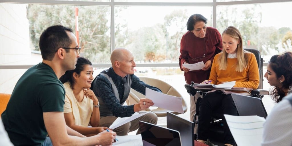 businessmen and businesswomen sit in a group with laptops having a discussion