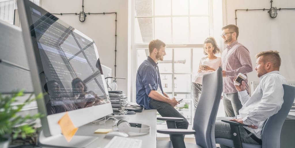 technology workers are collaborating in an office space with a computer screen showing data in the foreground