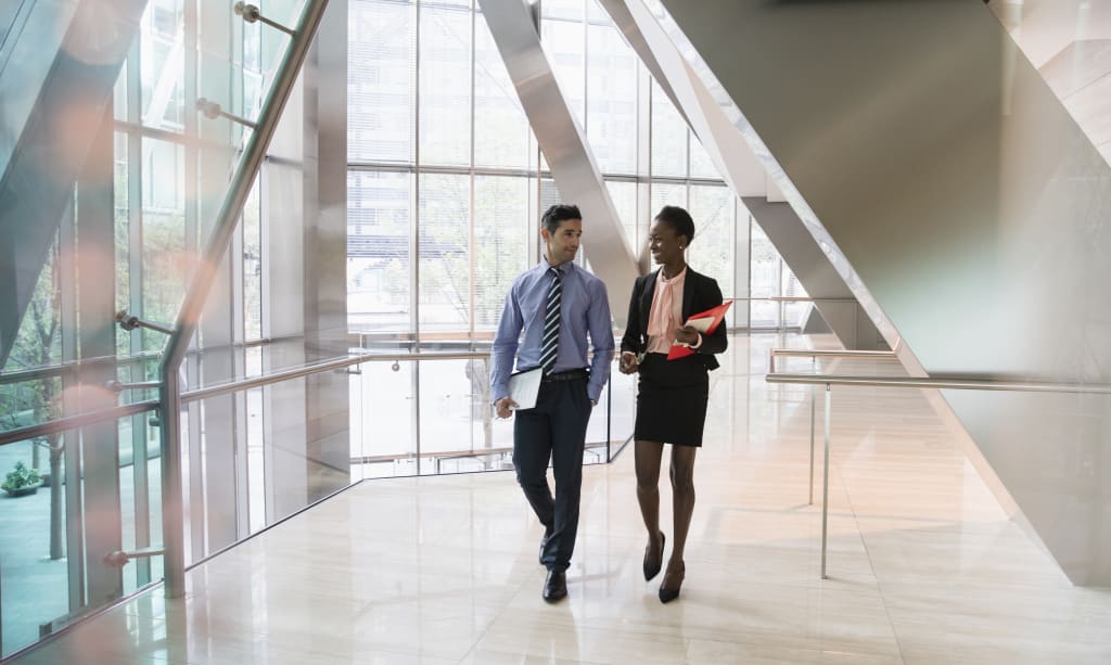 corporate businessman and businesswoman walking and talking in modern office lobby