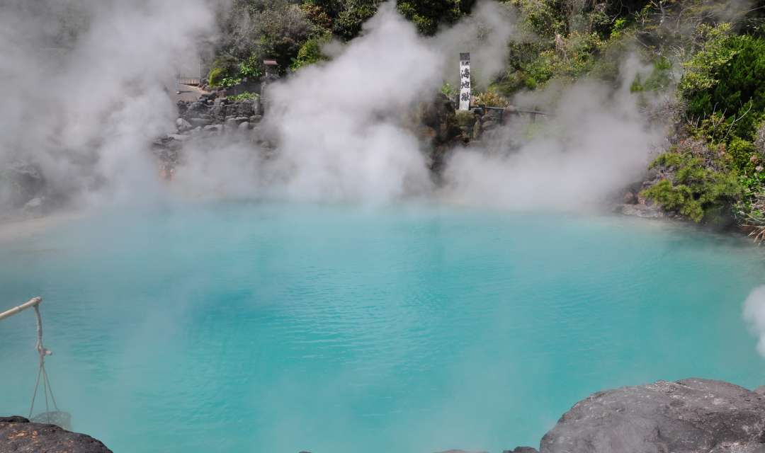 Blue steaming onsen pool with rocks in foreground