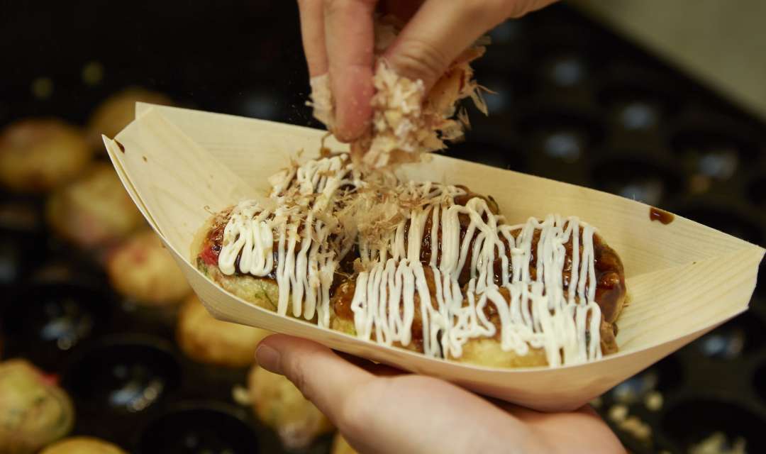 hands picking up takoyaki in a bowl