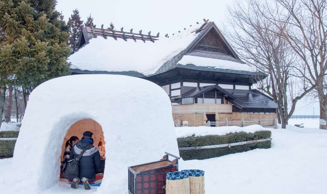 people inside a kamakura igloo next to a house on snowy ground