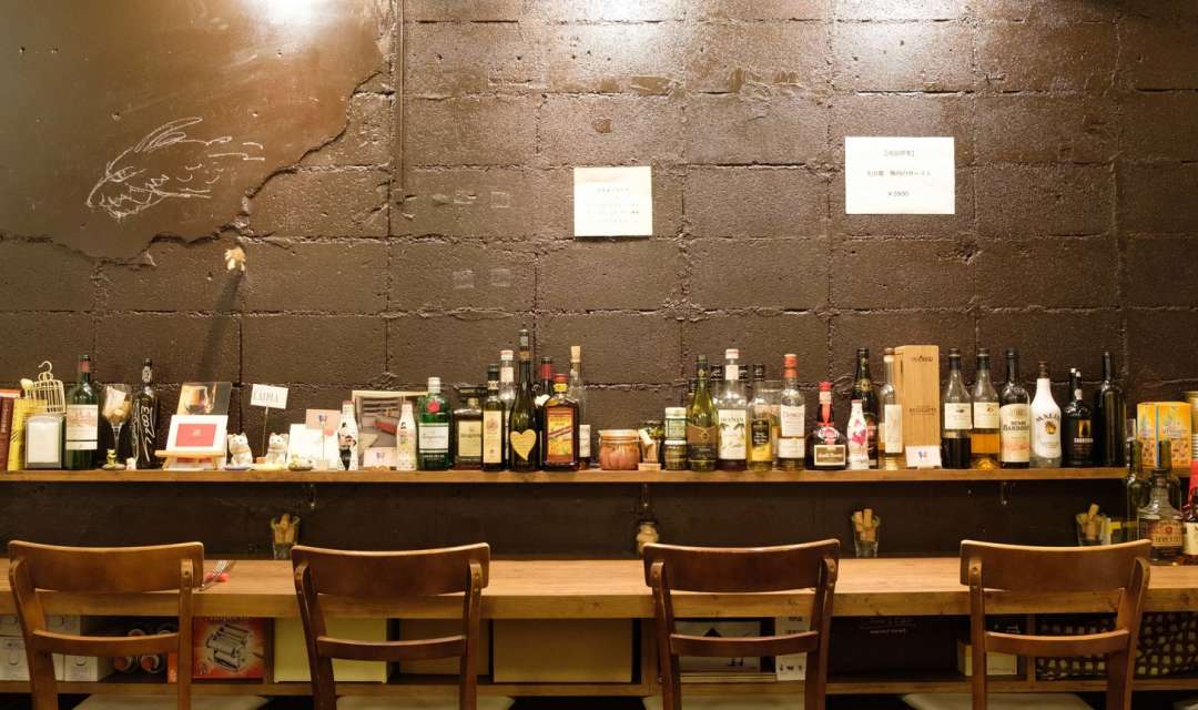 a row of chairs and a counter table behind a shelf with bottles of alcohol