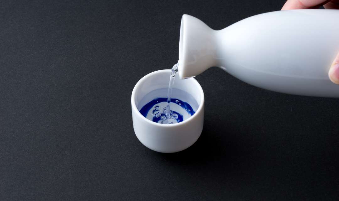 a bottle of sake being poured into a ceramic cup